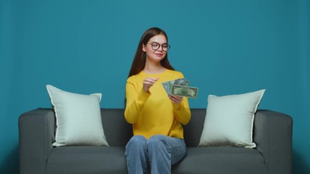 金持ちの少女は ドルの現金散乱 ソファの上に座ってお金を投げる 豪華なライフスタイル 寛大さ 高品質4K映像 — ストック動画