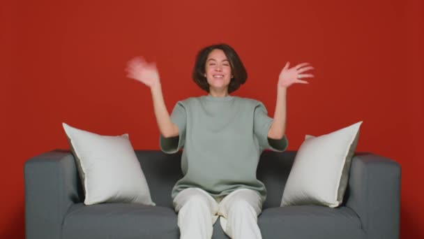 En vacker flicka med en välkomnande gest viftar med handen mot kameran. Begreppet dejting. Den röda bakgrunden isolerad. — Stockvideo