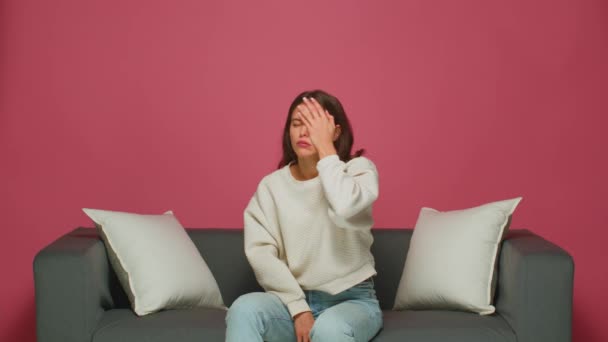 Funny emotional young girl resents, makes facepalm gesture, feeling shame, sitting on sofa, watching movie or series — Stock Video