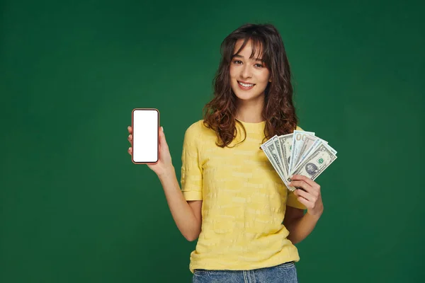 Usmívající se mladá dívka drží peníze v ruce, telefon s prázdnou makléřskou obrazovkou, těšit finanční zisk. Inzerát aplikace e-bank — Stock fotografie