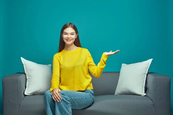 Friendly modern young girl showing by hand palm advertising space with good sale offer, sitting on couch Stock Image