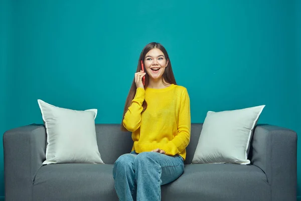 Podekscytowana młoda dziewczyna wykonująca lub odbierająca telefon, ciesząca się miłą rozmową z przyjacielem, siedząca na kanapie Zdjęcia Stockowe bez tantiem