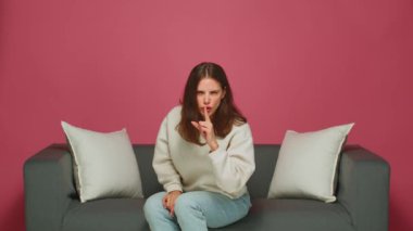 Ciddi, güzel, sessiz bir jest yapan genç bir kız, sessiz kalmak, sır tutmak, kanepede oturmak istiyor.