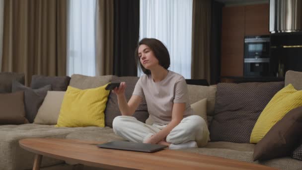 Mujer joven aburrida y cansada viendo programas de televisión aburridos, cambiando canales por control remoto, sentado en el sofá — Vídeos de Stock