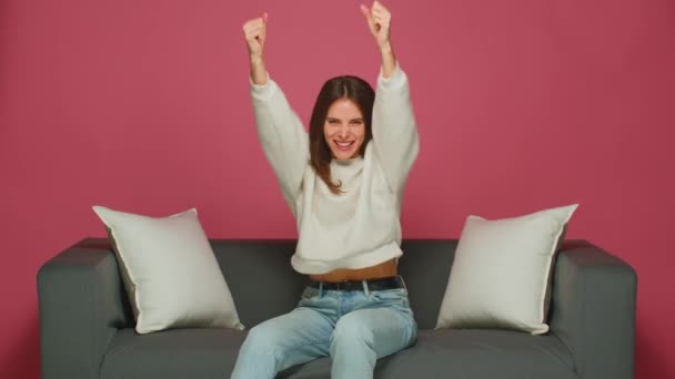 Jovem alegre se sentir eufórico, mulher animada levantando as mãos felizes com a vitória ou sucesso, gritando, sentado no sofá — Vídeo de Stock