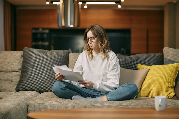 Upset young girl hold papers, bills worried about financial problem, bank debt, sitting on couch. Lack of finances Royalty Free Stock Images