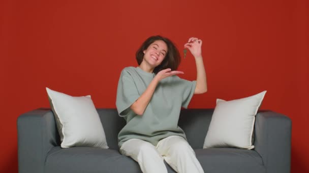 Glada unga flicka visa nycklar till nya hem, sitter på soffan. Hyra, hypotekslån, fastighetsinvesteringar — Stockvideo