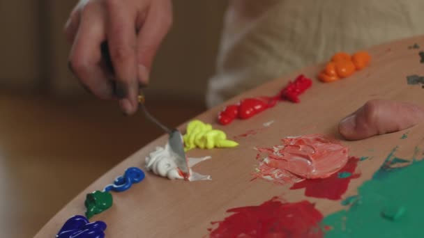클로즈업을 하는 남성 미술가는 팔레트를 손에 들고 아크릴 페인트를 팔레트 칼로 혼합하여 미술 작품에 사용 할 색깔을 준비 한다. 현무암 — 비디오
