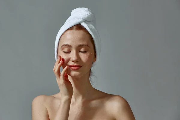 Menina feliz em toalha toque pele rosto perfeito aplicando creme nutritivo, hidratante nas bochechas. Conceito de tratamento da pele — Fotografia de Stock