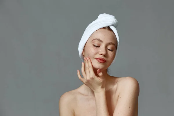 Młoda kobieta z idealną skórą, nagimi ramionami, ręcznikiem na głowie, dotykająca masującej twarzy. Naturalne piękno, pielęgnacja skóry Zdjęcie Stockowe