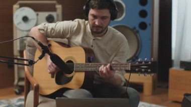 Kulaklıklı, gitar çalan, bilgisayar ekranına bakan, mikrofon kullanarak müzik kaydeden modern bir adam. ProRes kodlayıcısı