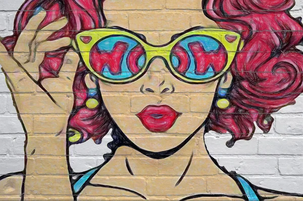 Street art. Very close-up drawing of a woman's face drawn with chalk. The woman has red hair and wears sunglasses in which the word 