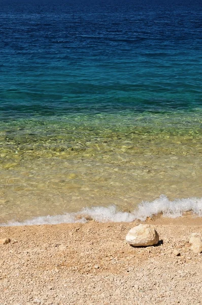Пляж с волнами и большим камнем — стоковое фото