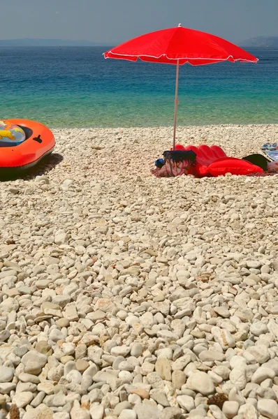 Plaj çakıl taşları ve bir yaz gününde kırmızı şemsiye — Stok fotoğraf