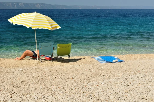 Uomo che riposa sotto l'ombrellone giallo sulla spiaggia — Foto Stock