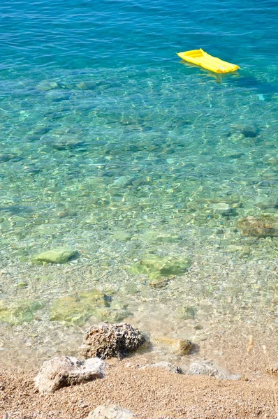 Beautiful beach with stones and yellow airbed — Stock Photo, Image