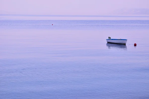 Piccola barca da pesca solitaria galleggiante sulla superficie piana del mare — Foto Stock