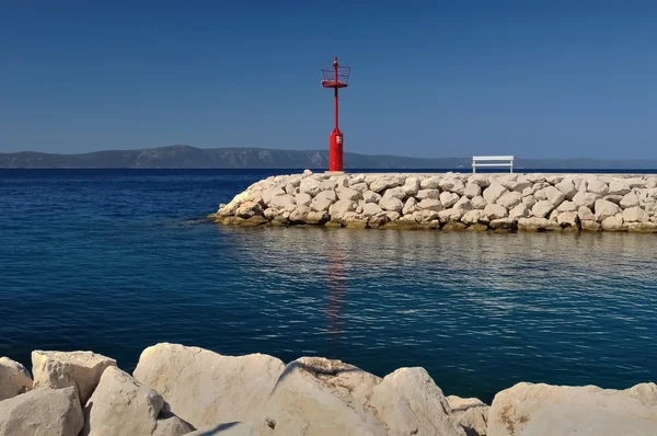 Red lighthouse in port with stones and white bench — Stock Photo, Image