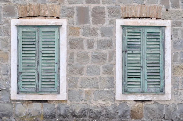 Två gamla fönster med blå slutna fönsterluckor på ett gammalt hus Stockbild