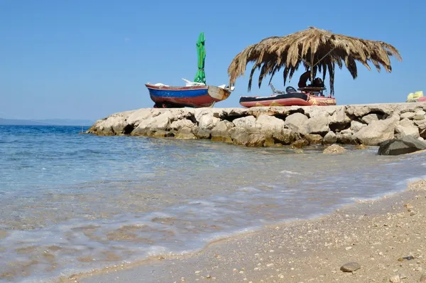 Praia de Podgora com rochas, palma e barco. Croácia — Fotografia de Stock