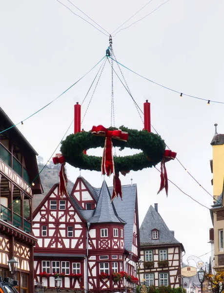 Almanya, Bacharach 'ta bir caddenin üzerinde asılı kırmızı mum ve yaylı yeşil Noel çelengi.