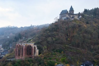 Almanya 'da sisli bir sonbahar gününde Bacharach şehrine bakan Wernerkapelle' in yukarısındaki ağaçlarla kaplı Stahleck Kalesi..