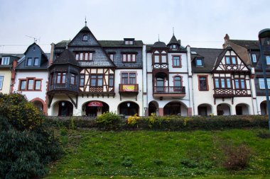 Almanya 'nın Bacharach şehrinde bulutlu bir sonbahar gününde yeşil çimenli bir tepenin üzerinde birbirine bağlı binalar sırası.