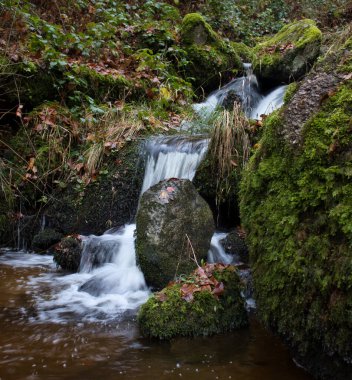 Large rocks in a small waterfall at Gaisholl on a fall day in the Black Forest of Germany.