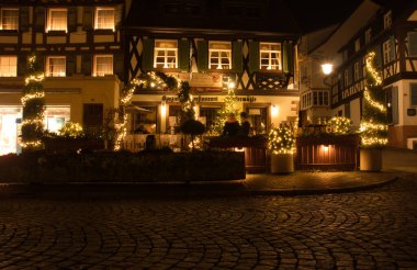 Gengenbach, Germany - December 13, 2020: Restaurant in half-timbered building with Christmas lights on the corner of a cobblestone road on a fall night in Gengenbach, Germany.