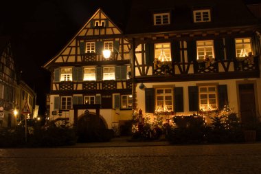Gengenbach, Germany - December 13, 2020: Half-timbered house with green shutters and teddy bears hanging on the wall under the windows on a fall night in Gengenbach, Germany.
