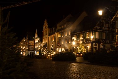 Gengenbach, Germany - December 13, 2020:  Street with half-timbered houses lit up at night with Christmas trees on the sidewalk in Gengenbach, Germany.