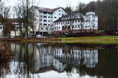 Enkenbach-Alsenborn, Almanya - 31 Aralık 2020: Almanya 'nın Enkenbach-Alsenborn kenti yakınlarındaki soğuk bir kış gününde küçük bir gölette yansıması olan beyaz huzurevi.