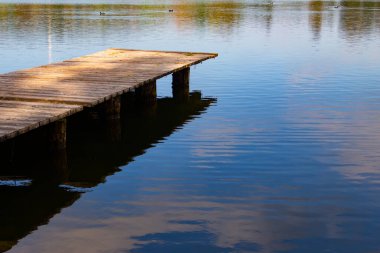 Göl kenarındaki boş iskele ve gökyüzünü kopyalama alanı ile yansıtan su.