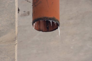 Kırmızı plastik drenaj borusunda buz saçakları eriyor.