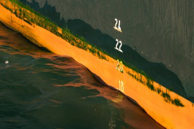 Waves at a black and orange ship hull with white draft marking