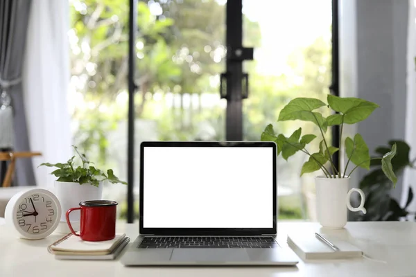 Laptop with red coffee mug and plants pot and white clock on white table indoor