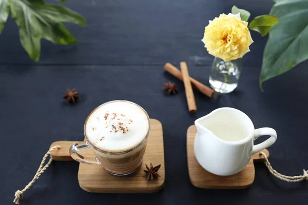 グラスカップのラテコーヒーとダークテーブルの上にバラの花とミルクピッチャー — ストック写真
