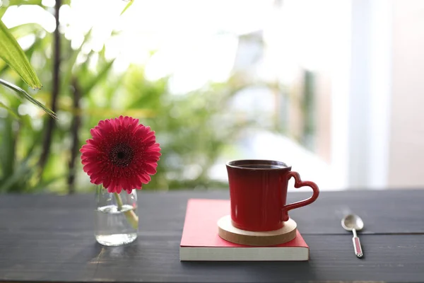 Red coffee mug and red gerbera flower on black table surface