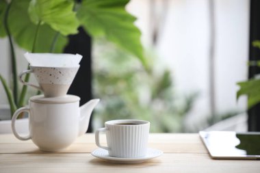 Beyaz kahve fincanı ve seramik kahve demlik ve tablet ahşap masada.