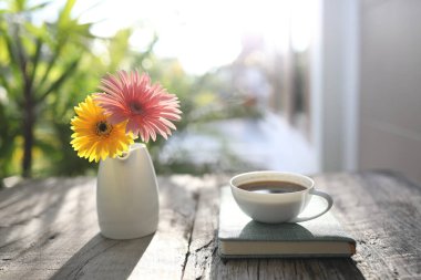 Gerbera çiçekli beyaz kahve fincanı ve defter.