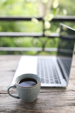 Kahve fincanı ve dizüstü bilgisayar balkondaki ahşap masada.