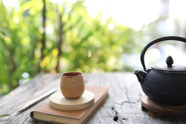 Metal çaydanlık ve ahşap masanın üzerinde kahverengi defter olan bambu bardak.