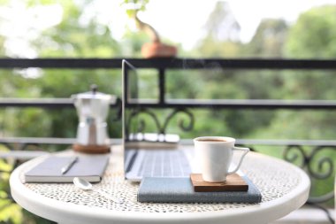 Metal masada beyaz kahve fincanı, defterler ve dizüstü bilgisayar.