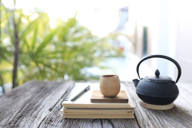 Tahta masanın üzerinde kahverengi defter olan bambu kabı ve metal çaydanlık.