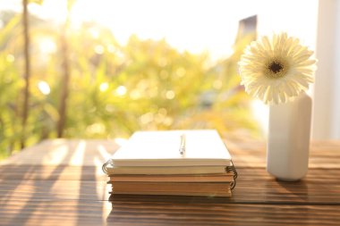 Vazoda gerbera çiçeği ve eski kahverengi ahşap masa üzerinde defterler.