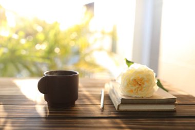 Kahverengi kupa, gül ve ahşap masadaki defterler.