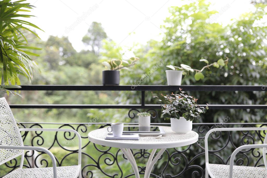 Coffee cup and and tablet and plant pot on white metal table at balcony outdoor
