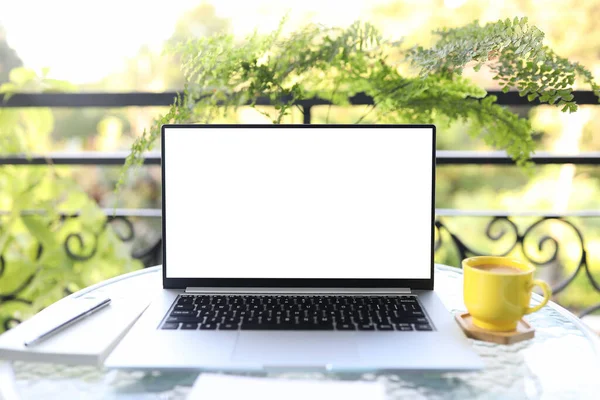 Laptop front view and yellow coffee cup with notebooks on white glass table outdoor