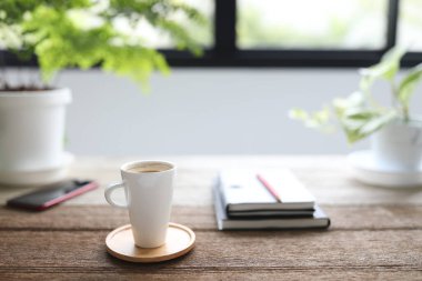 Uzun kahve fincanı, defterler, telefon ve ahşap masaya demlik.