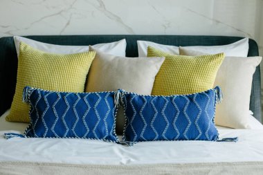 Yatakta farklı renk ve boyutlarda yastıklar düzgünce dizilmiş. İç tasarım..